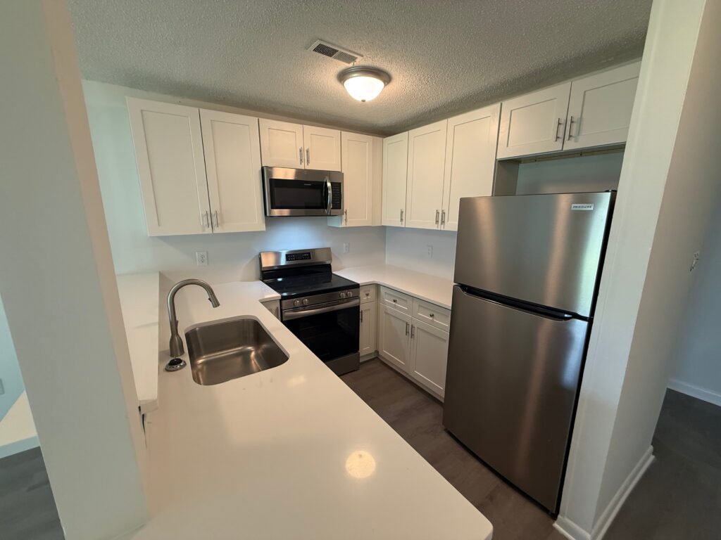 Modern kitchen with white cabinets, stainless steel appliances, built-in microwave, electric stove, double sink, and overhead lighting—enjoy these stylish amenities at Delmont Townes.