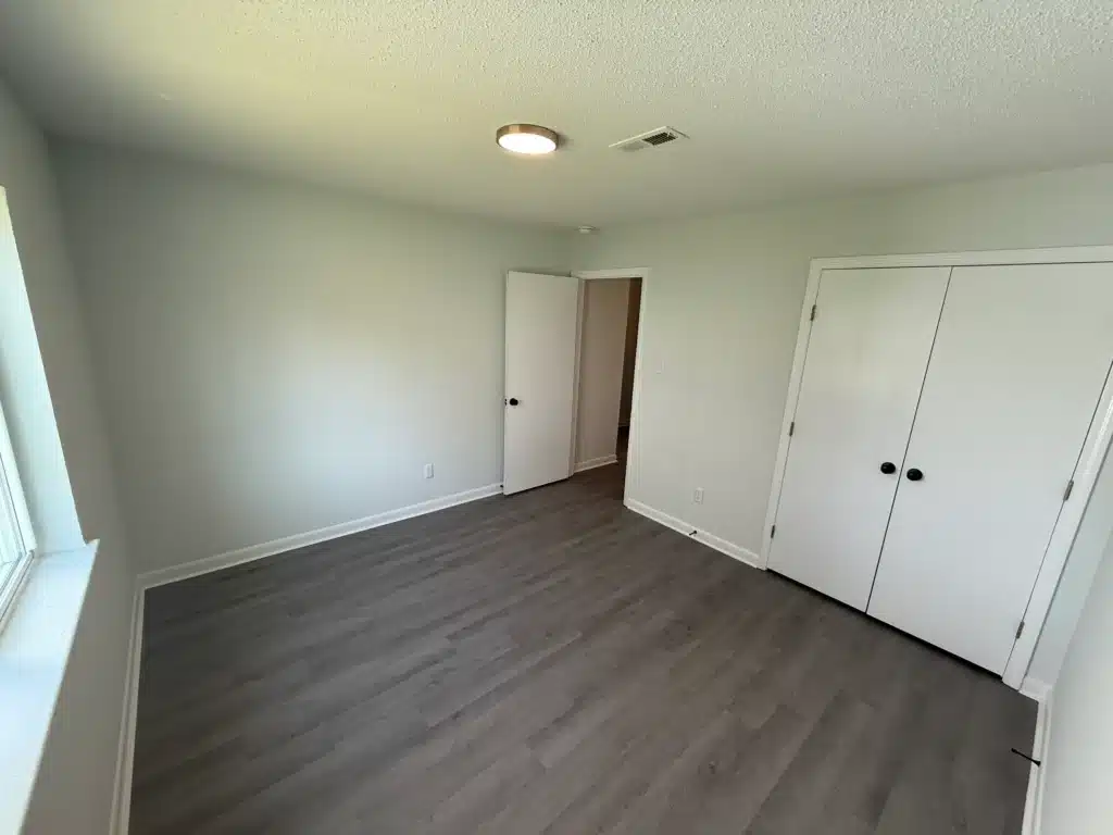 Bright and airy empty room at Gallery - Delmont Townes featuring light gray walls, a white ceiling, vinyl plank flooring, a window, an open door, and double closet doors.
