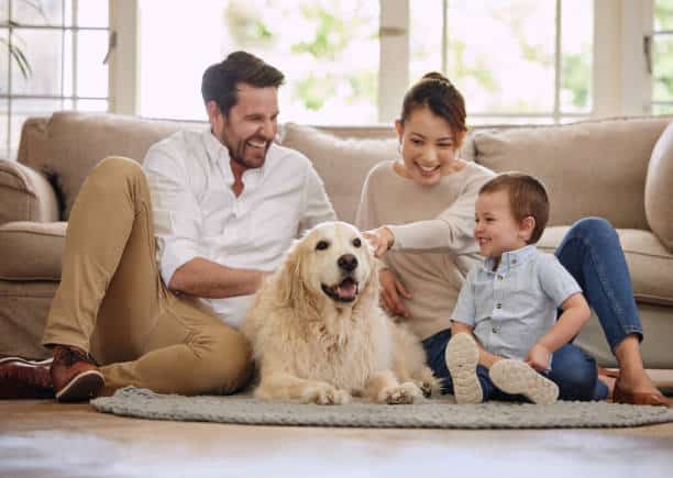 A man, woman, young boy, and golden retriever sit together on a rug in a Delmont Townes living room, all smiling and enjoying the pet-friendly amenities.